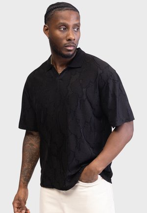 Polo noir à manches courtes présentant un motif texturé, un col côtelé et une coupe décontractée. Le tissu semble doux avec des détails subtils.