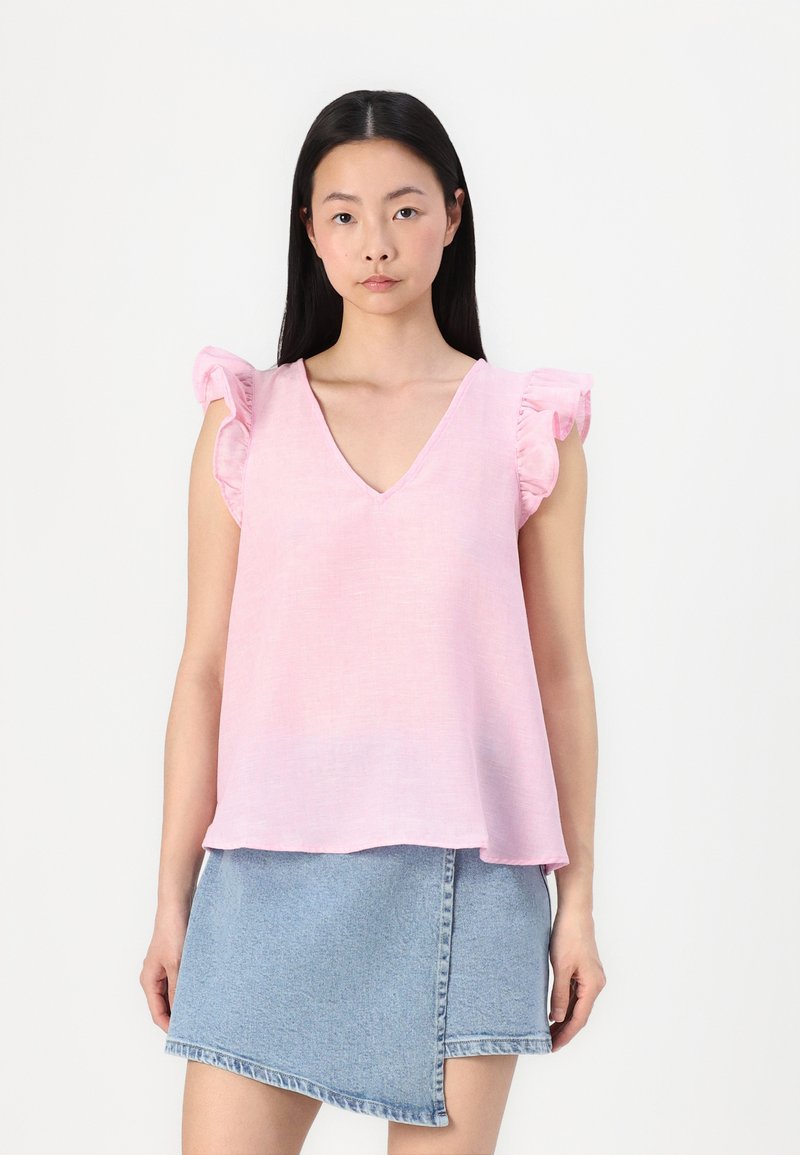 Top rosa senza maniche con scollatura a V e spalline arricciate, abbinato a una gonna di jeans con orlo diagonale.