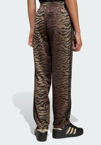 Smeđe-crne hlače s tiger prugama, s elastičnim pojasom, bočnim prugama i glatkom teksturom, uparene s crno-bež tenisicama.
