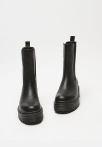 Black ankle boots made of smooth leather with a chunky rubber sole, elastic side panels, and pull tabs for easy wear.