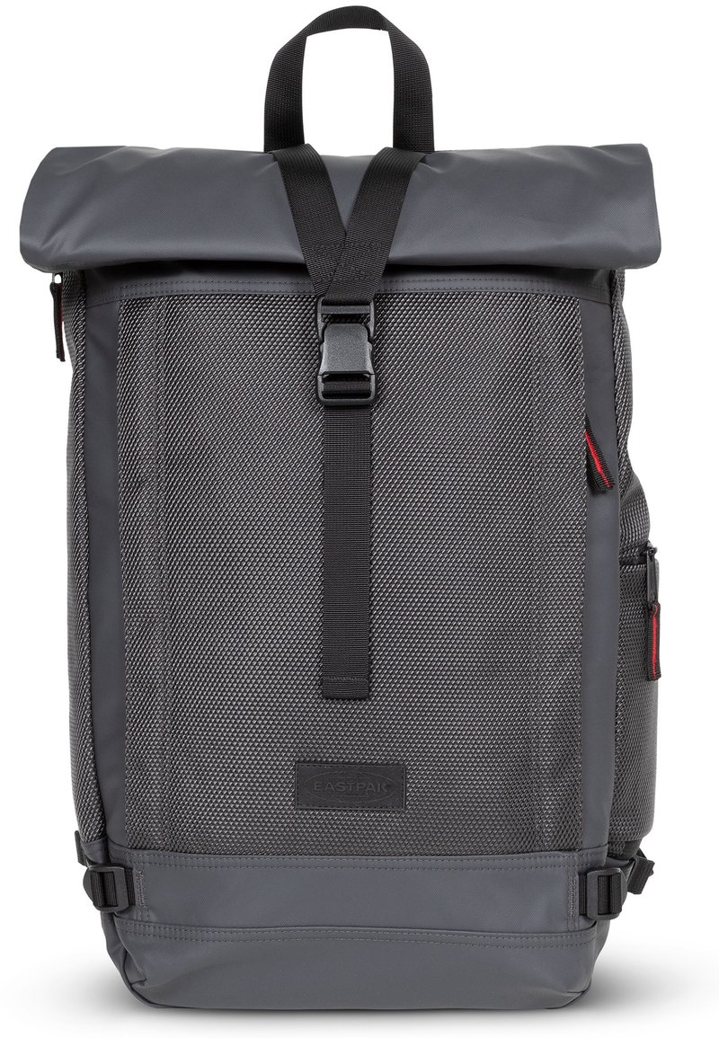 Sac à dos gris à rabat, en tissu texturé, avec des bretelles réglables et une fermeture à boucle. Il est équipé de poches latérales et d'un patch de marque.