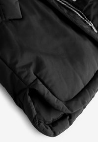 Giacca a vento nera con finitura opaca, texture trapuntata, chiusura frontale con zip e colletto ripiegato. Tessuto morbido e liscio e design slanciato.
