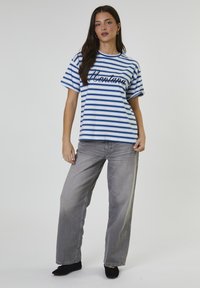 Camiseta de manga corta a rayas azules y blancas con el texto "Montana"; combinada con jeans de pierna ancha grises y zapatos negros. Tejido de algodón suave.