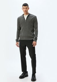 Suéter gris de canalé con cuello con cremallera, combinado con pantalones negros y zapatos negros. Textura suave y diseño ajustado. Estilo minimalista.