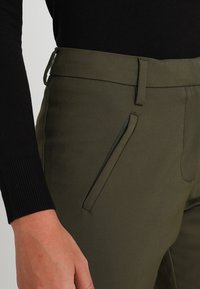 Olivgröna byxor med slim fit, sidofickor med svarta detaljer och en mjuk textur. Designade med bältes-loopar och knappstängning.