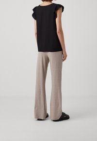 Musta toppi, jossa on röyhelöhihat, yhdistetty vaalean beigeihin leveälahkeisiin housuihin teksturoidusta kankaasta. Asun täydentävät sandaalit.