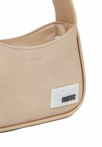 Beige lærred håndtaske med en glat læderrem, med et hvidt mærketag med "RE" og teksturerede accenter. Tekstureret overflade og sømme synlige.