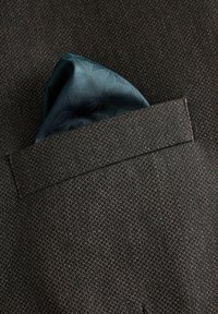 Veste de costume en tissu marron foncé avec un tissage texturé, comportant un mouchoir de poche teal plié placé dans une poche poitrine.