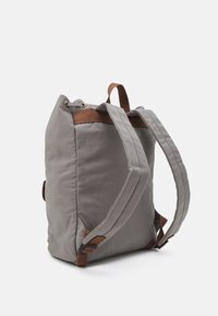 Grå tygryggsäck med bruna remmar, i fyrkantig form och med texturerad yta. Har detaljer i guld och justerbara axelremmar.