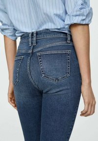 Jean en denim bleu taille haute avec une texture lisse, deux poches arrière et un design classique avec coutures.