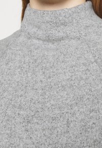 Szary sweter z wysokim kołnierzem, wykonany z miękkiej, teksturowanej dzianiny. Posiada dopasowany krój oraz subtelne tonalne wariacje przędzy.