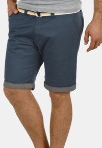 Shorts en coton bleu marine avec un ourlet roulé, dotés de poches latérales et d'une ceinture à rayures jaunes. Texture lisse et design ajusté.