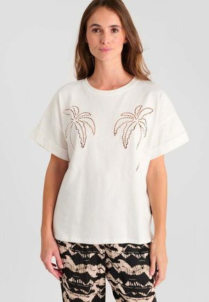 T-shirt bianca di cotone con maniche corte e design ritagliati a forma di palma sul davanti, abbinata a pantaloni neri e beige a fantasia.