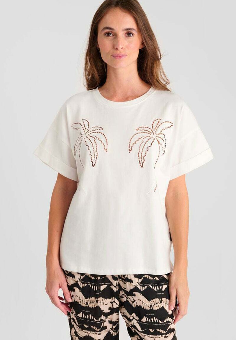 T-shirt bianca di cotone con maniche corte e design ritagliati a forma di palma sul davanti, abbinata a pantaloni neri e beige a fantasia.