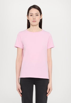 Lichtroze katoenen t-shirt, korte mouwen, ronde halslijn, losse pasvorm, gladde textuur, gecombineerd met zwarte jeans op een neutrale achtergrond.