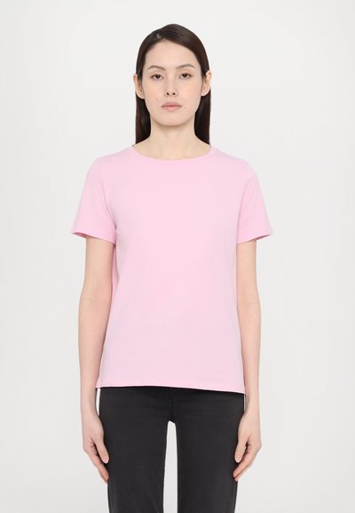 T-shirt en coton rose clair, à manches courtes, avec un col rond, de coupe décontractée, texture lisse, associé à un jeans noir sur un fond neutre.
