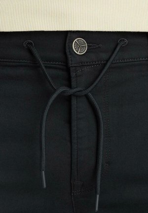 Pantaloni neri con coulisse frontale e bottone logo metallico. Tessuto liscio con dettagli di cucitura e design aderente.