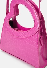 Roze handtas met een glanzende afwerking, voorzien van een uniek hartvormig handvat, krokodillenpatroon en een ritsvak.