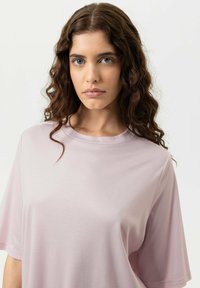 T-shirt oversize rose clair à manches courtes avec une texture lisse et un col rond, présenté sur un fond neutre.