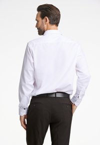 Witte langemouwen overhemd met een rugpand, gecombineerd met donkere broek. Heeft knoopmanchetten en een soepele, kreukvrije stof.