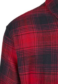 Chemise à carreaux rouge et noir en tissu texturé, présentant un motif à carreaux et un col classique.