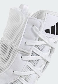 Weißer Sportschuh mit Mesh-Obermaterial, gepolstertem Schaft und flachen weißen Schnürsenkeln. Verfügt über ein schwarzes Logodetail an der Seite. Weiche textile Elemente.