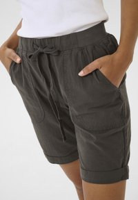 Shorts noirs à cordon de serrage fabriqués dans un tissu léger. Comprend deux poches latérales, des ourlets roulés et une taille élastique. Texture lisse.