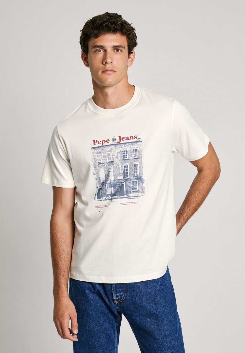 Bílá bavlněná trička s modrým grafickým potiskem znázorňujícím budovu, s nápisem "Pepe Jeans!" a uvolněným střihem. V kombinaci s modrými džínami.