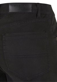 Pantaloni in denim neri con una texture liscia, dotati di una tasca posteriore e di un'etichetta in pelle sul punto vita. Sono visibili dettagli cuciti.
