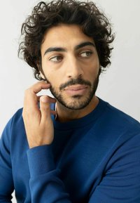 Zila kreklvieta ar garām piedurknēm, gluda tekstūra un pieguļošs dizains. Mīksta auduma un smalka mirdzuma, ko nēsā persona ar cirtainiem matiem.