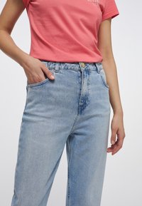 Světlé modré vysoké pasu džíny vyrobené z denimu, s klasickým designem pěti kapes a zlatým uzávěrem. Měkká textura a rovný střih.
