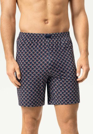 Mann trägt dunkelblaue Boxershorts mit kleinem rotem und weißem Fahrradmuster, steht vor einem einfarbigen Hintergrund.