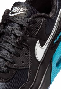 Nærbillede af sort Nike Air Max-sneaker med hvid swoosh-logo, sorte snørebånd og blå sål-accents.