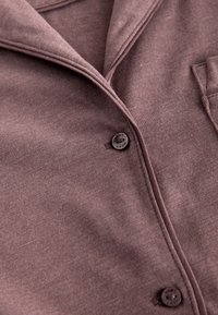 Camicia marrone con bottoni, realizzata in tessuto morbido, con colletto classico, tasca applicata e due bottoni scuri sul davanti.