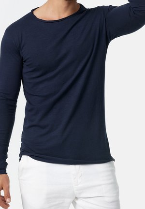 Chemise bleu marine à manches longues, tissu doux, coupe décontractée, encolure ronde, avec une légère texture et un détail de couture subtil à l'ourlet.