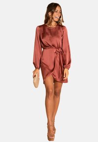 Robe en satin couleur rouille avec des manches longues, un détail à lien à la taille et une jupe drapée. Présente une texture lisse et une silhouette décontractée.