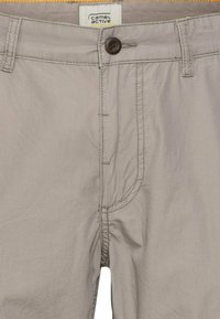 Helle graue Hose mit glatter Oberfläche, einzelne braune Knopfverschluss und kontrastierendes orangenes Taillenband. Verfügt über subtile Nähte.