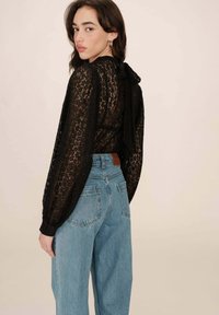 Zwarte kanten blouse met lange pofmouwen en een strik aan de achterkant. Gecombineerd met lichtblauwe high-waisted denim jeans, met achterzakken.