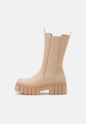 Botte Chelsea beige mi-mollet avec semelle à crampons épaisse et panneaux latéraux élastiques pour un enfilage facile, conçue pour un usage décontracté ou urbain.