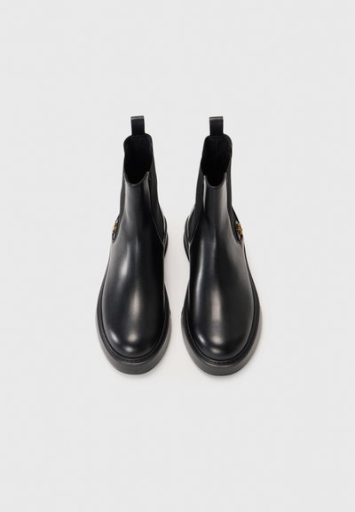 Svarta läderankelboots med en slät yta, rund tå, elastiska sidopaneler och en dragflik bak. Minimalistisk design och diskret metallisk detalj.
