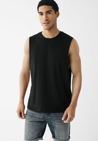 T-shirt sans manches noir en coton, avec un col rond et une coupe décontractée. Associé à un short en denim bleu clair.