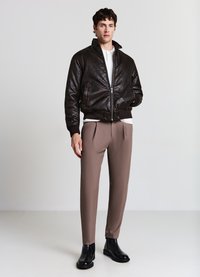 Braune Leder-Bomberjacke mit Reißverschluss, gerippten Bündchen und Kragen. Kombiniert mit hellbraunen, maßgeschneiderten Hosen und schwarzen Stiefeletten.