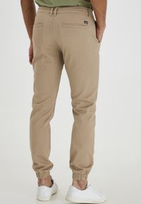 Pantalons de jogging beiges avec des poignets élastiques, poches latérales et arrière, fabriqués à partir d'un tissu lisse. Doté d'une petite étiquette de marque sur la ceinture.