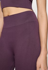 Lila bordázott sporttop és magas derekú leggings. Az anyag sima textúrával és illeszkedő kialakítással rendelkezik, széles derékrésszel.