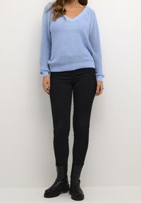 Pullover a maglia di un azzurro chiaro con scollatura a V, tessuto strutturato e polsini arrotolati, abbinato a jeans neri aderenti e stivali neri alla caviglia.