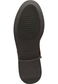 Suela de zapato de goma negra con surcos texturizados y perforaciones circulares, con la marca "GEOX PATENTE ITALIANO" cerca del talón.
