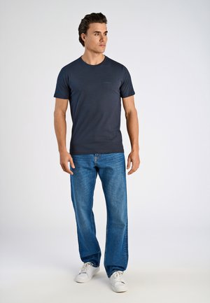 Marineblauwe crewneck t-shirt van een zachte stof, gecombineerd met lichtblauwe rechte jeans. Model draagt witte sneakers. Eenvoudig ontwerp, geen patronen.