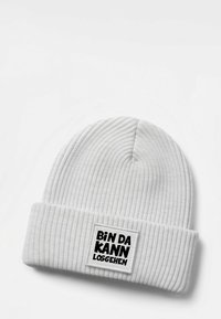 White knitted beanie with a ribbed texture and a folded cuff, featuring a rectangular patch with black text "BIN DA KANN LOSGEHEN".
