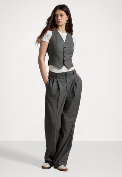 Vesta gri cu nasturi și buzunare, asociată cu pantaloni gri cu talie înaltă. Tricou alb dedesubt. Material neted și design croit.