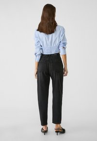 Camisa a rayas azul y blanca recortada con cintura elástica, combinada con jeans negros de tiro alto; bolsillos traseros visibles, usados con tacones negros.